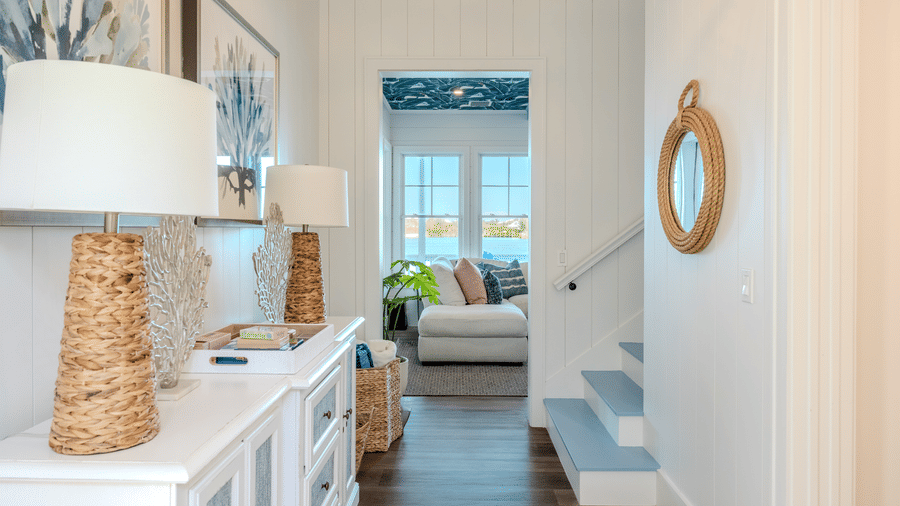 A view from the foyer toward the living room, featuring a white sideboard with coral-inspired lamps and a glimpse of light blue stairs.