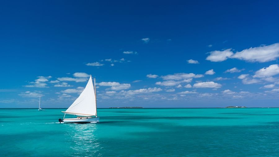 A sailboat gliding across calm turquoise waters under a clear blue sky, with the ocean stretching to the horizon in the background | Abaco Inn