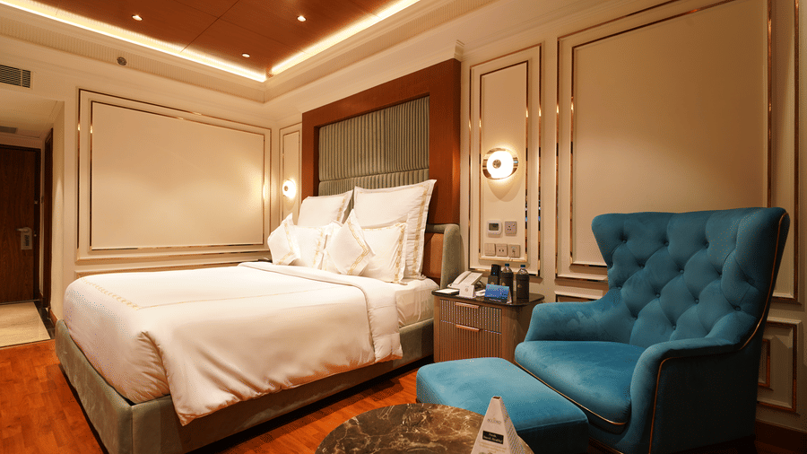 An elegant hotel bedroom with a king size bed, teal armchair, side table, and elegant panelling at Accord Metropolitan.