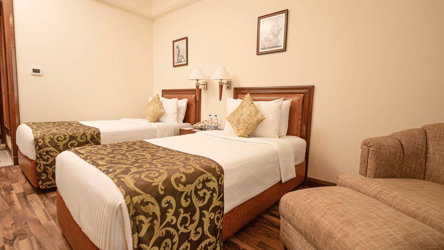 The Superior Room with twin bed at Accord Metropolitan with crisp linens, 2 wall art, and a sofa chair.