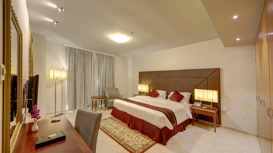 A spacious suite featuring a large double bed, a wooden desk with a chair, and elegant white marble flooring - Al Manar Grand Hotel Apartment, Bur Dubai
