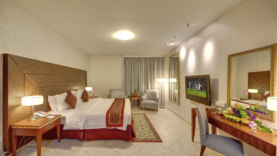 A large bedroom suite offers a king size bed, a vanity mirror, a television, and a comfortable armchair - Al Manar Grand Hotel Apartment, Bur Dubai