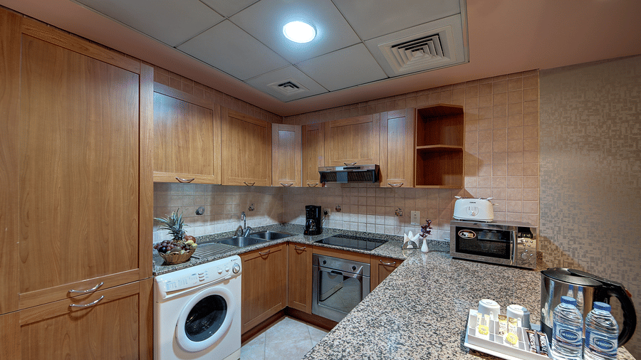 A compact kitchen area includes wooden cabinets, a washing machine, a kettle, and a granite worktop - Al Manar Grand Hotel Apartment, Bur Dubai