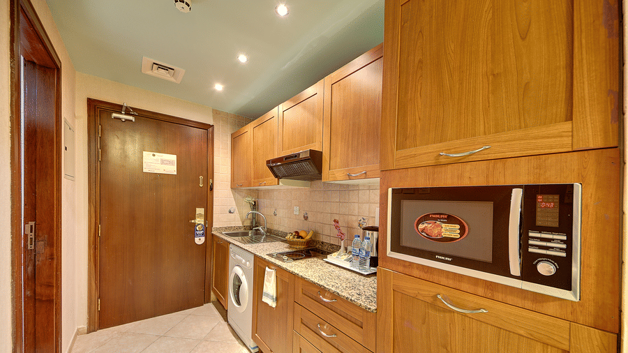 A functional kitchen area is equipped with wooden cabinetry, a microwave, a stove, and an integrated washing machine - Al Manar Grand Hotel Apartment, Bur Dubai