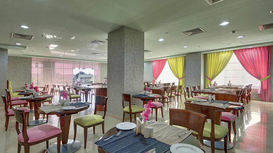 The hotel restaurant features several dining tables with colourful chairs and bright pink and yellow curtains - Al Manar Grand Hotel Apartment, Bur Dubai