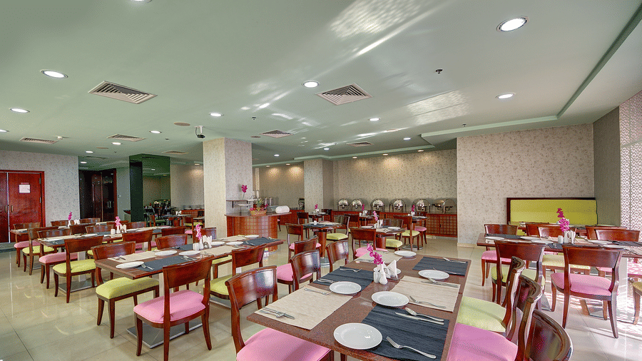A brightly lit hotel restaurant features rows of dining tables with colourful pink and green chairs - Al Manar Grand Hotel Apartment, Bur Dubai