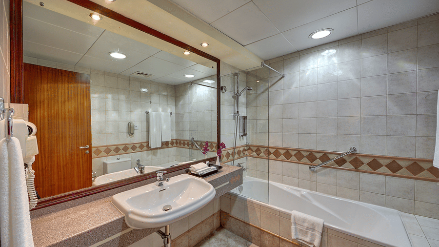 A clean bathroom with a white bathtub, a large wall mirror, and neutral-coloured tiled walls - Al Manar Grand Hotel Apartment, Bur Dubai