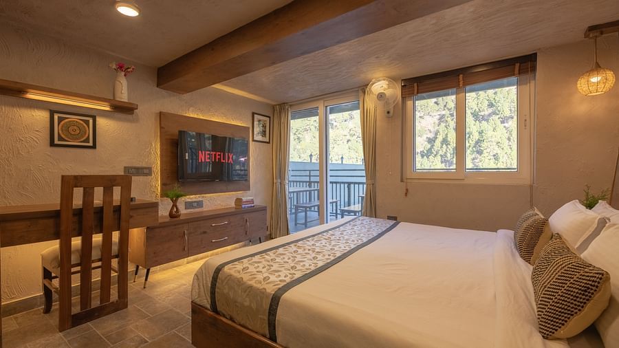 Room with double bed, TV, balcony doors, wooden beams on the ceiling, and soft lighting.