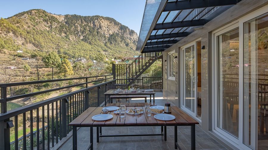 Outdoor dining tables set on a narrow balcony with views of green hills and a clear sky.