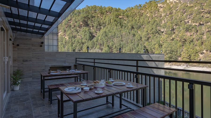 Outdoor dining tables set on a narrow balcony with views of green hills and a clear sky.