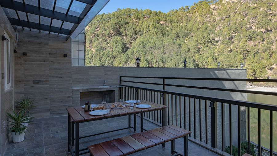 Outdoor dining tables set on a narrow balcony with views of green hills and a clear sky.