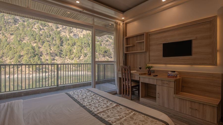 Room with double bed, TV, balcony doors and soft lighting.