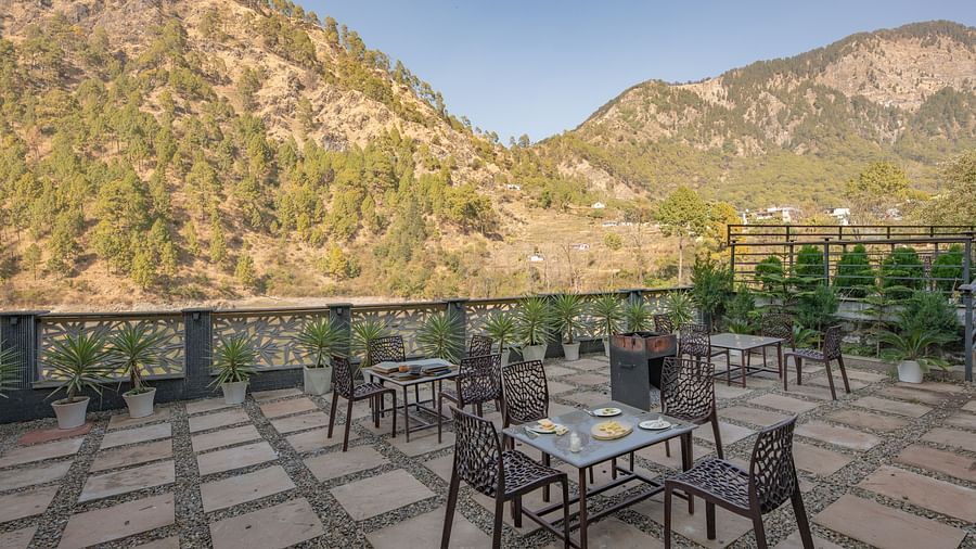 Outdoor dining tables set on a narrow balcony with views of green hills and a clear sky.
