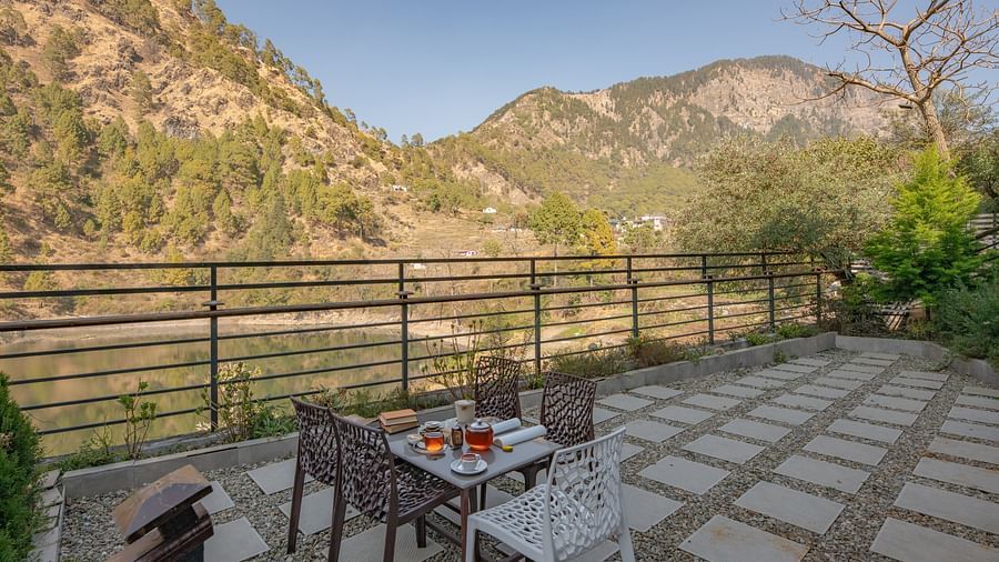 Outdoor dining tables set on a narrow balcony with views of green hills and a clear sky.