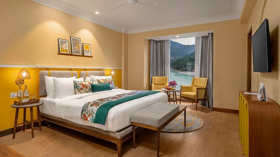  The room features a king-size bed with a plush headboard and comofrtable bedding. Armchairs by the window, offering a scenic view of the mountains. The room also includes a wooden desk, a television, and a ceiling fan. 