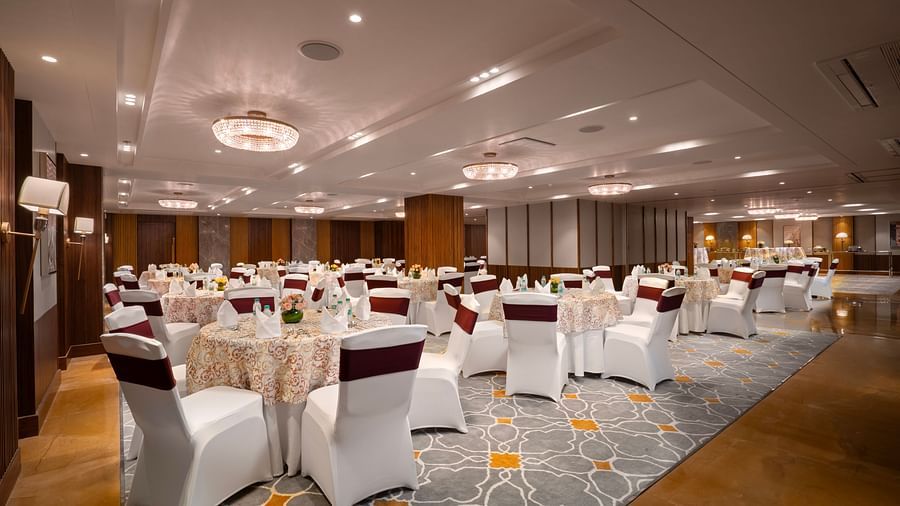 A spacious conference hall with round tables covered in tablecloths and chairs. and the room is decorated with chandeliers and wall lamps.