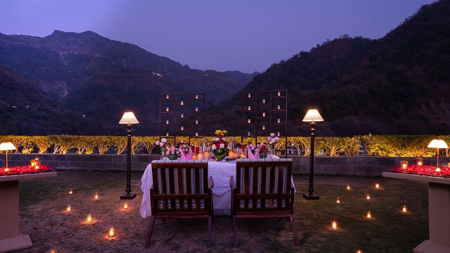 A dinner setup outdoors with a table adorned with candles and flowers,he backdrop is a beautiful mountain range at dusk.