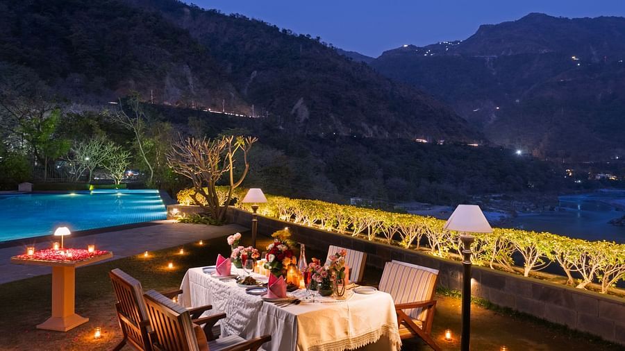 A dinner setup by a pool with mountains in the background. The table is adorned with candles and flowers.