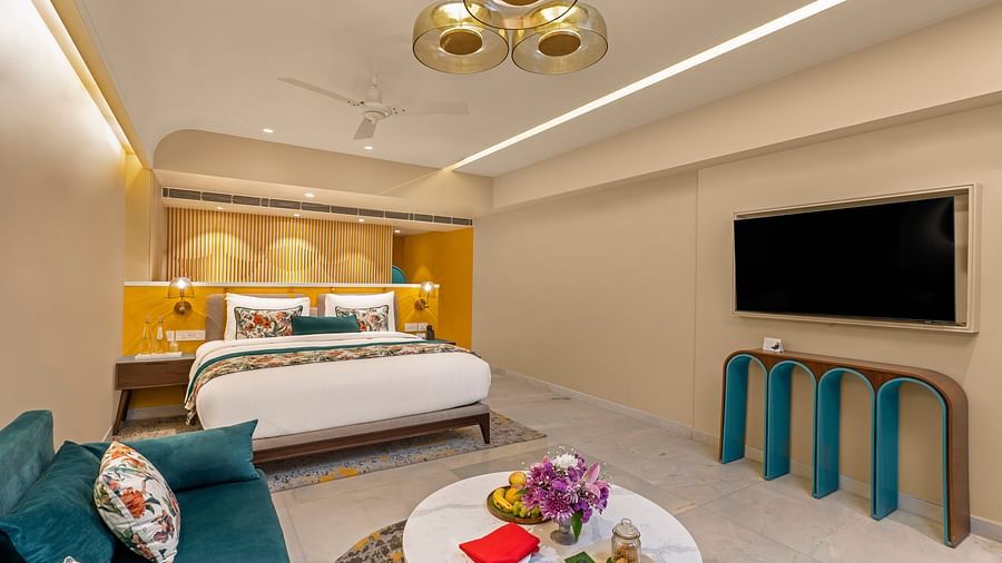 A n image of luxurious hotel suite with king bed, sofa, coffee table, and stylish decor.