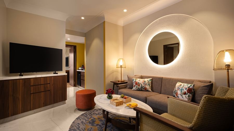 A modern and spacious living room with a comfortable sofa, a coffee table, and a large circular mirror with LED lighting. 