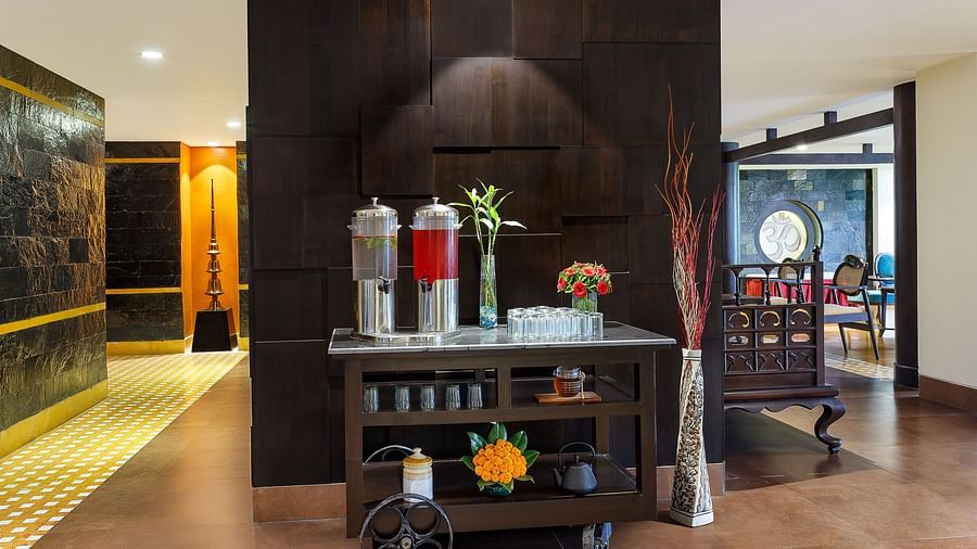 hotel lobby with a beverage station in the center. There are coffee and tea dispensers, as well as a cart with snacks and refreshments.