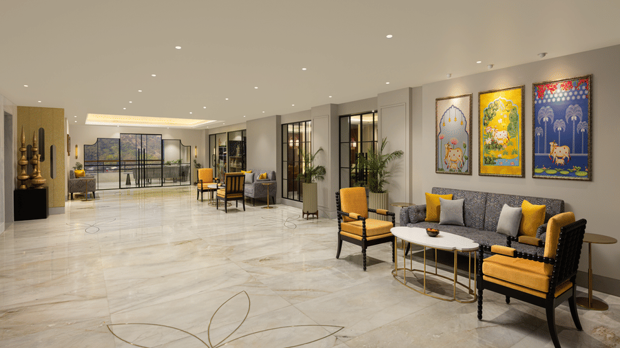 Spacious hotel atrium with marble floors, yellow-accent seating, framed artwork, and warm recessed ceiling lighting creating a modern lounge ambience.