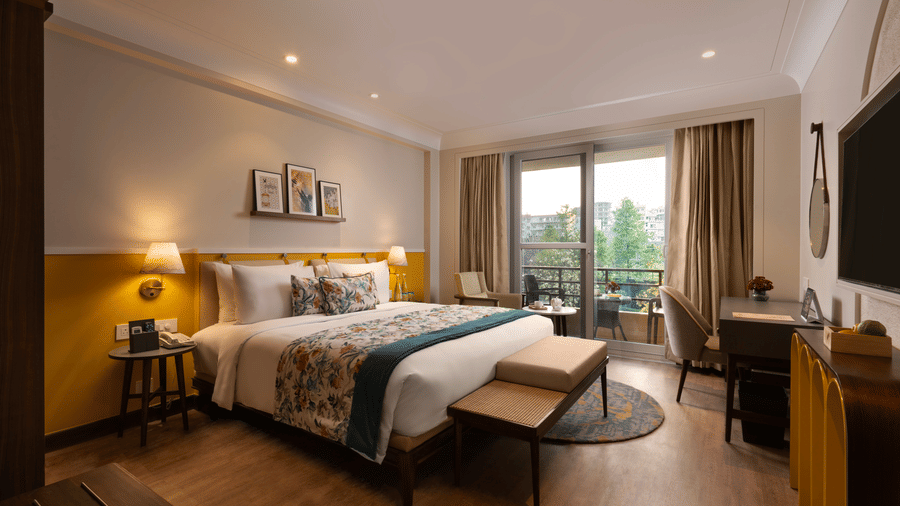 Elegant bedroom at Aloha on the Ganges Resort featuring a large bed with white linens, patterned pillows, warm lighting, balcony view, and cosy decor for a relaxing stay.