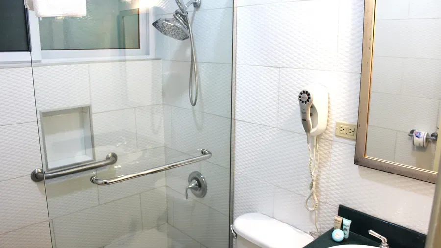 A contemporary bathroom includes a glass-enclosed shower, a toilet, and a white vanity with a sink and mirror | Deluxe Double Room | Altamont Court, Jamaica