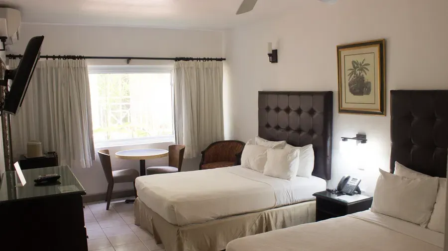 A spacious hotel room features two large beds, a sitting area with a table and chairs, and a window with curtains | Executive Double Room| Altamont Court, Jamaica