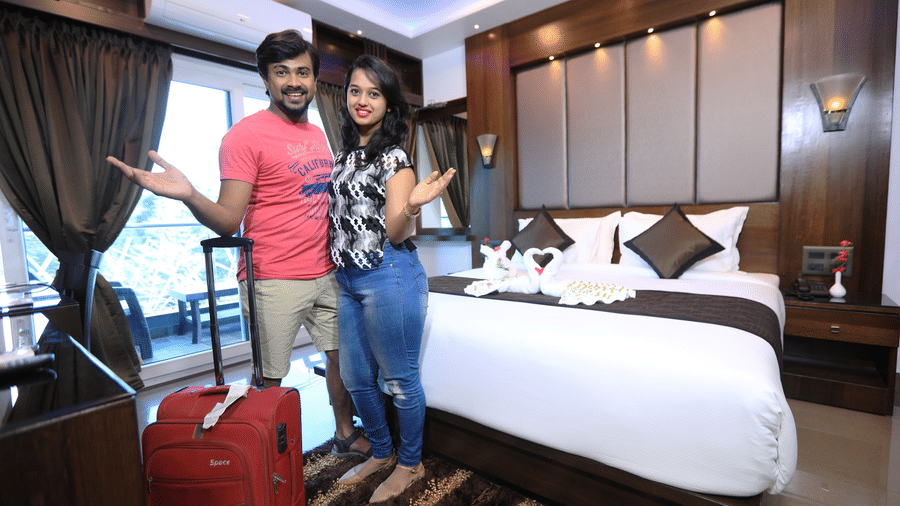 Image of a man and a woman standing in front of a bed with their luggage in front of them.