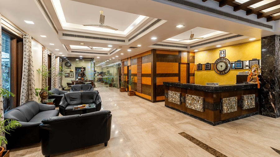 A wide-angle shot of the  hotel reception and lounge area showing modern black seating, bright ambient lighting, and a check-in desk - Amantra Comfort Hotel