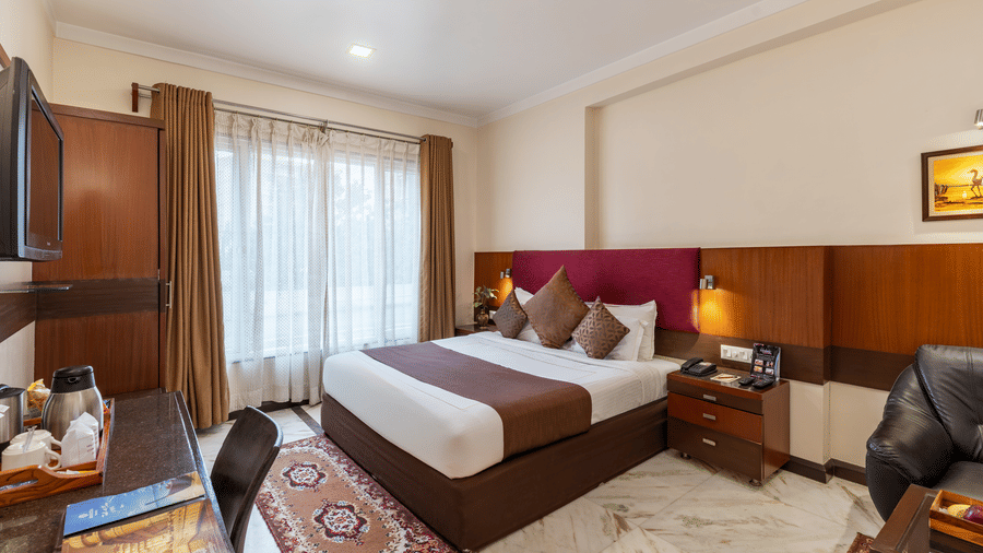 Full-view of the Royal Room featuring a king size bed with brown runners, a wooden work desk with white marble flooring - Amantra Comfort Hotel