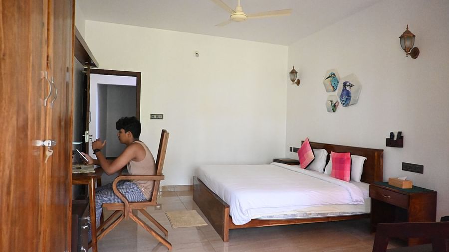 A boy sitting on a study table and a double bed behind him at 101 non ac Room at Ananda Holiday Home, Wayanad 2