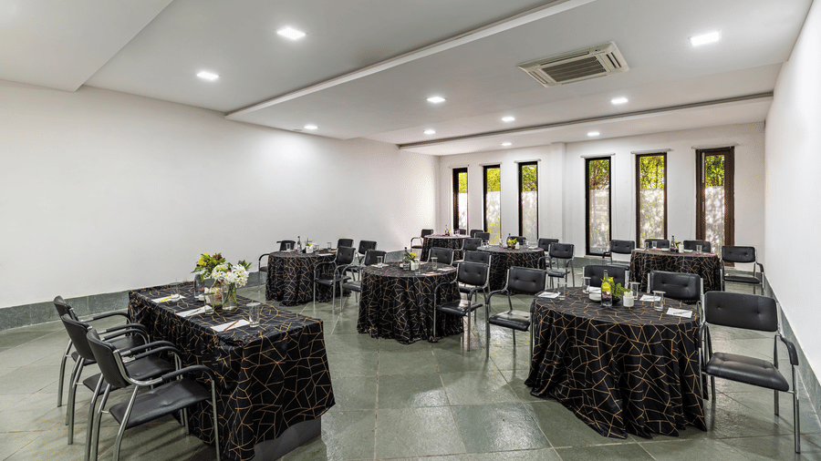 A conference room set up with multiple round tables covered in dark cloths | Anandam Jungle Retreat Resort, Udaipur