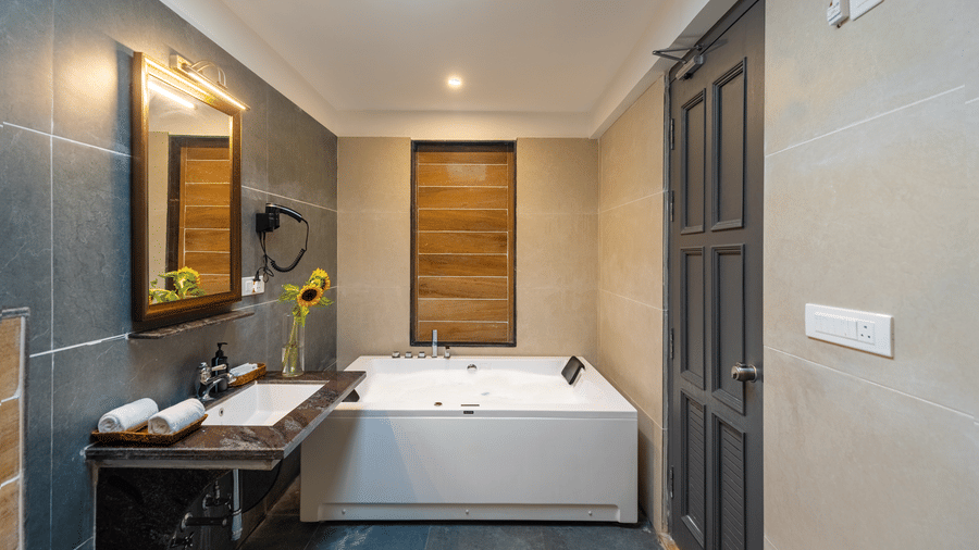 A bathroom with a Jacuzzi and a vanity unit under a warm light | Anandam Jungle Retreat Resort, Udapur