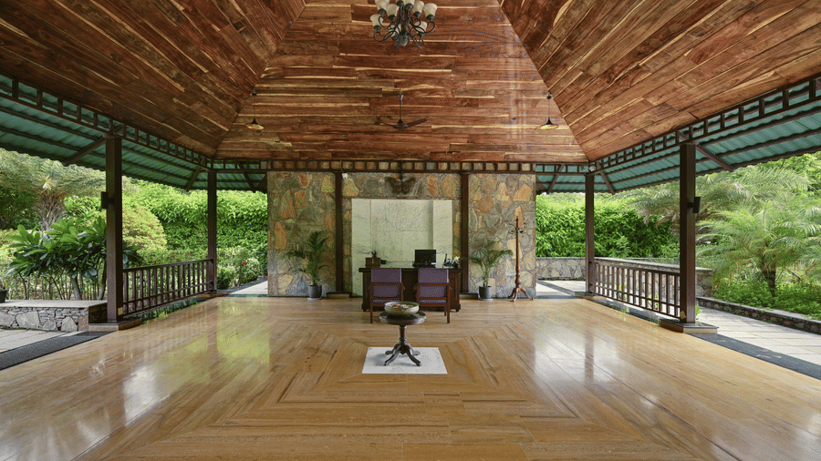 The interior of a large open-sided pavilion with polished wooden floors and a high timber ceiling | Anandam Jungle Retreat Resort, Udaipur