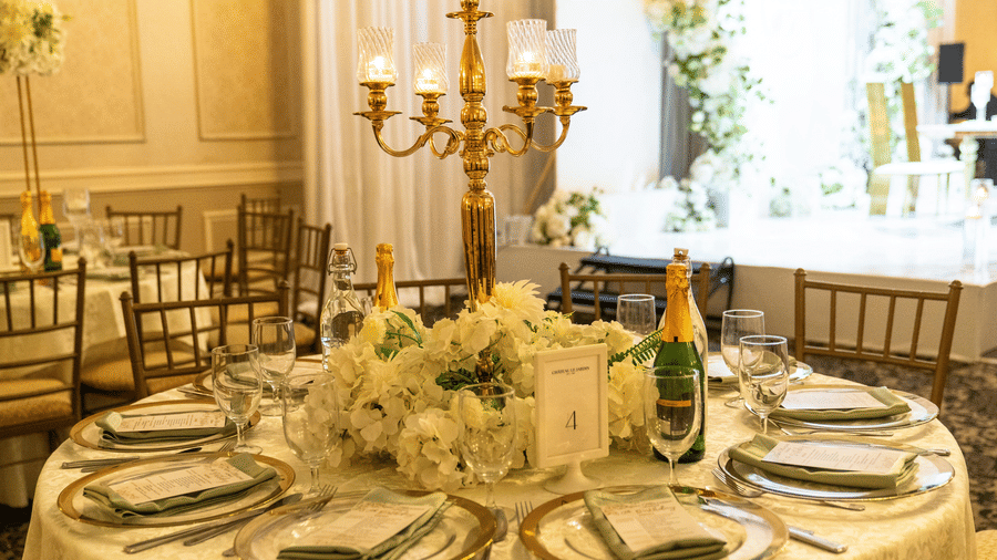 A formal dining table set for a wedding or event, featuring a large hydrangea centrepiece and a gold candelabra.