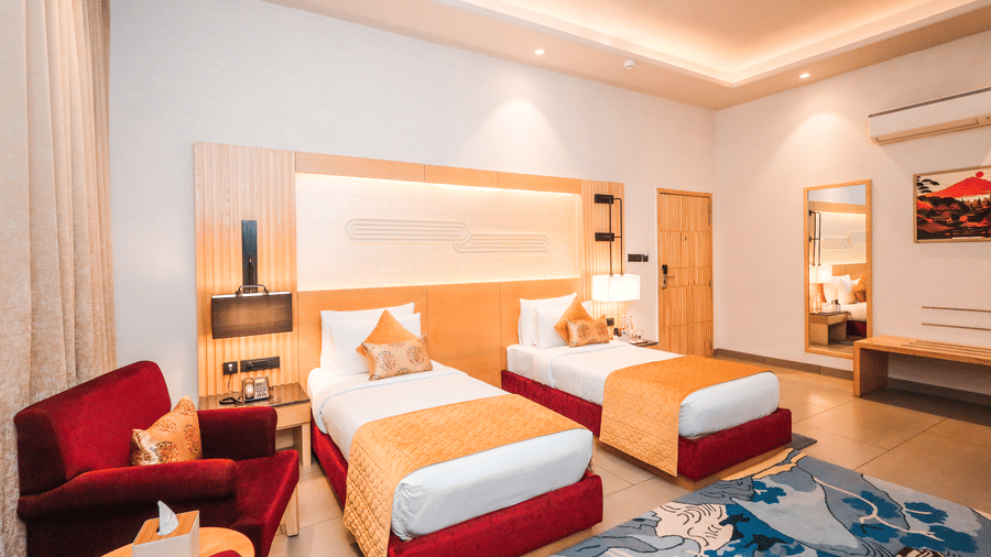 A room with two single beds, seating, lamps and wall art arranged around a central space at Ananta Spa & Resort, Jaipur.