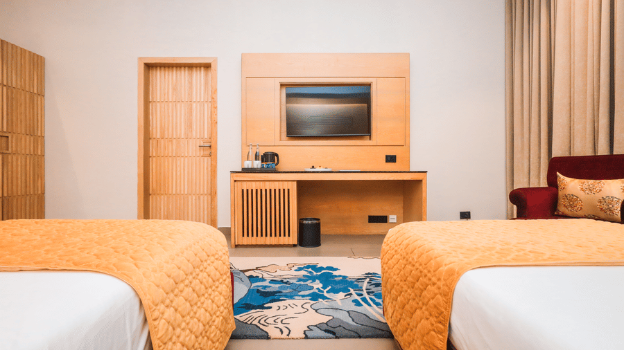 A room with two single beds, a television unit, seating and curtains placed around a central area at Ananta Spa & Resort, Jaipur.