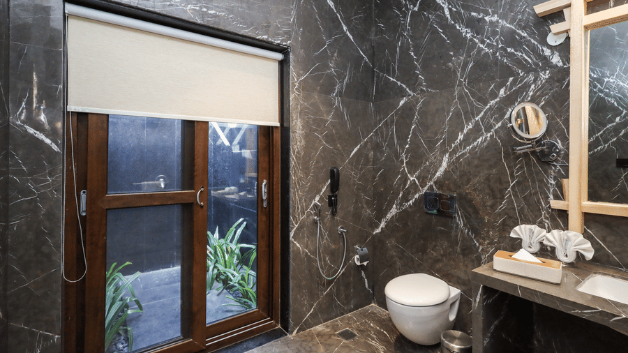A washroom shows a basin with a mirror, a toilet beside a window and tiled walls surrounding the area at Ananta Spa & Resort, Jaipur.