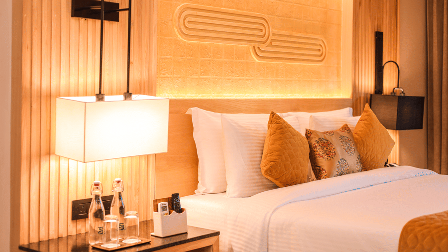 A room with a double bed, lamps, bottled water and side table viewed from one side at Ananta Spa & Resort, Jaipur.