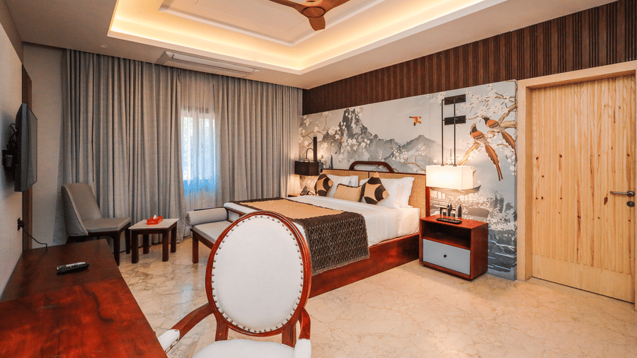 A room shows a bed with side tables, chairs with a table, curtains on windows and storage units along a wall at Ananta Spa & Resort, Jaipur.