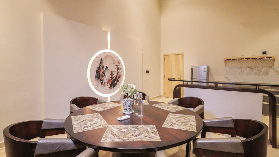 An interior shows a round dining table with chairs placed around it beside a counter and wall shelves at Ananta Spa & Resort, Jaipur.