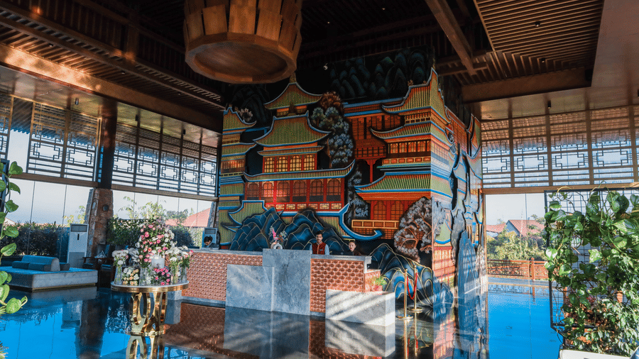 The brightly lit reception desk at Ananta Spa & Resort, Jaipur, stands in front of a colourful pagoda-themed mural and a large light.