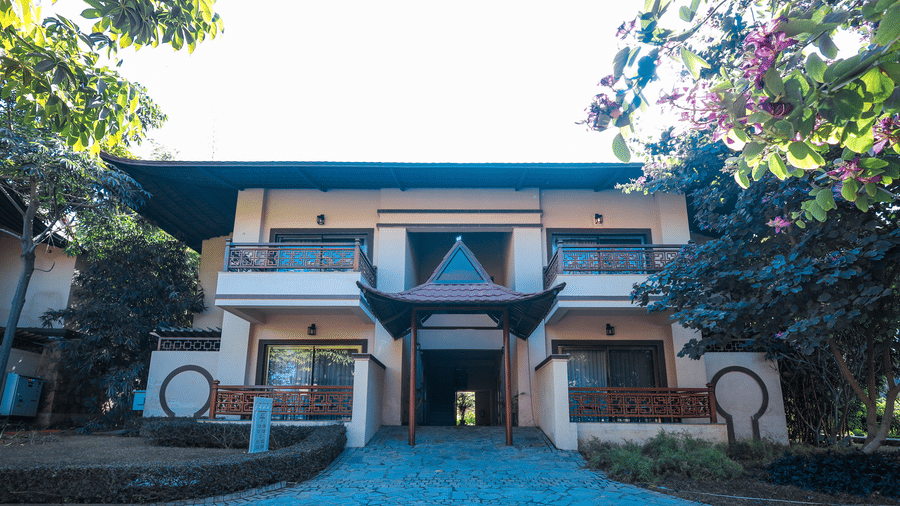 A building exterior with a central entrance, pathway and surrounding trees at Ananta Spa & Resort, Jaipur.
