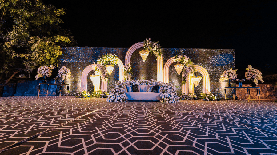Grand outdoor wedding stage with geometric floor at Ananta Spa & Resort, Jaipur, featuring floral arches at night.