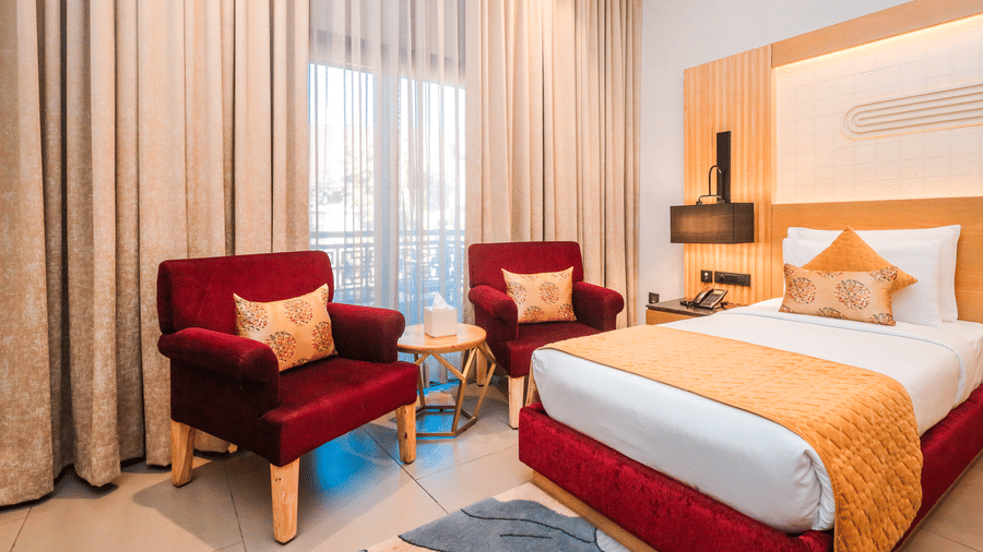 A room with a double bed, two chairs, curtains and lamps arranged around a central space at Ananta Spa & Resort, Jaipur.