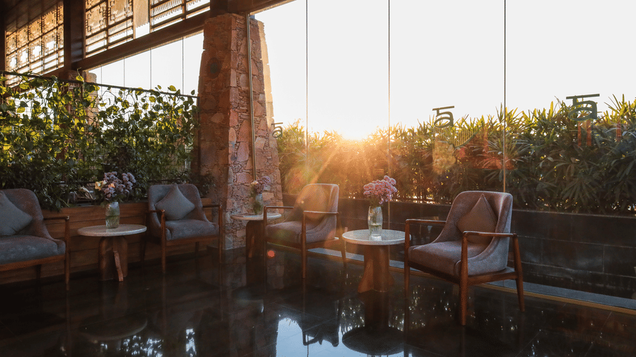 Sunlight shines into a bright, contemporary lounge at Ananta Spa & Resort, Jaipur, featuring dark floors and plush armchairs.