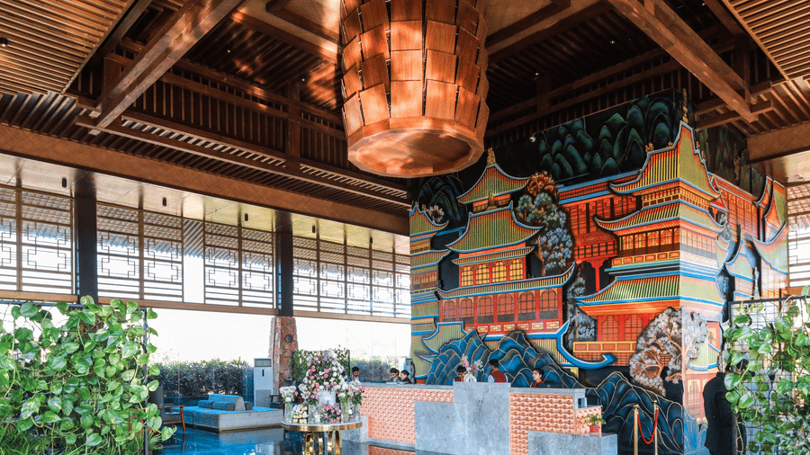 The reception area at Ananta Spa & Resort, Jaipur, features a pagoda mural, a copper-toned light fixture, and wooden ceilings.