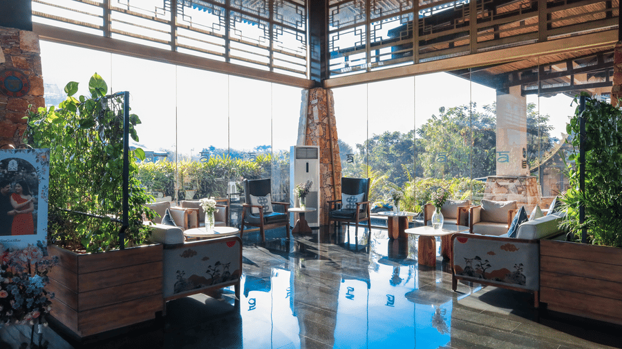 The sunny, open-plan lobby at Ananta Spa & Resort, Jaipur, features reflective dark floors, high ceilings, and surrounding greenery.